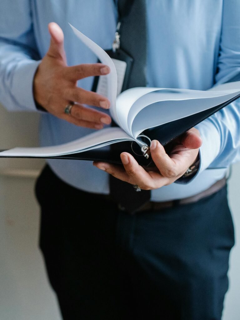 pexels-photo-5668837-5668837 A business professional in a suit flips through documents indoors, emphasizing formal work settings.