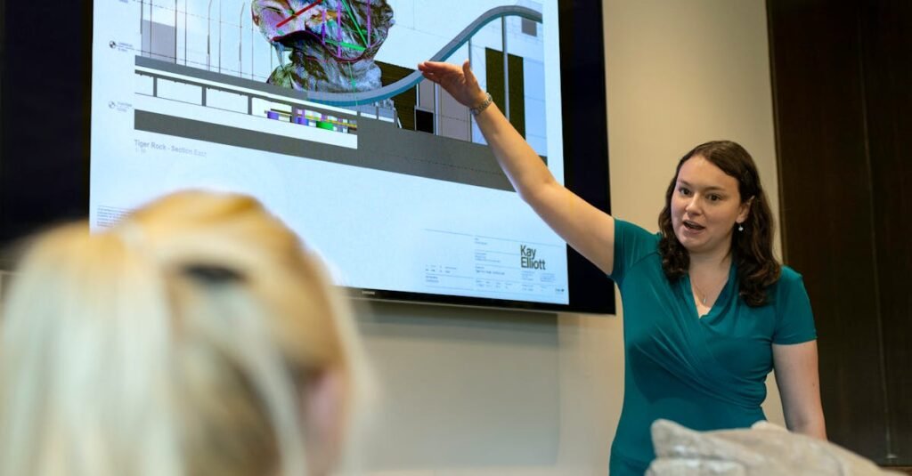 A female engineer delivers a presentation on rollercoaster design using a digital screen in an office.