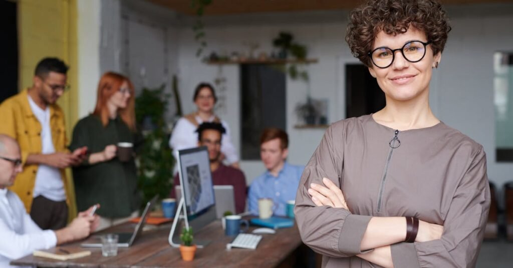 Smiling businesswoman with curly hair stands confidently in a modern office space with colleagues.