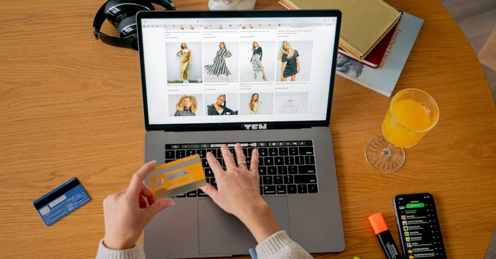 Hands holding credit card making online purchase on laptop at wooden desk with various items.