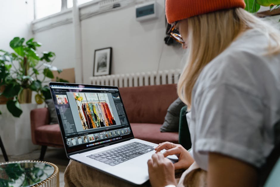 Woman using a laptop for photo editing in a cozy, plant-filled living room setting.