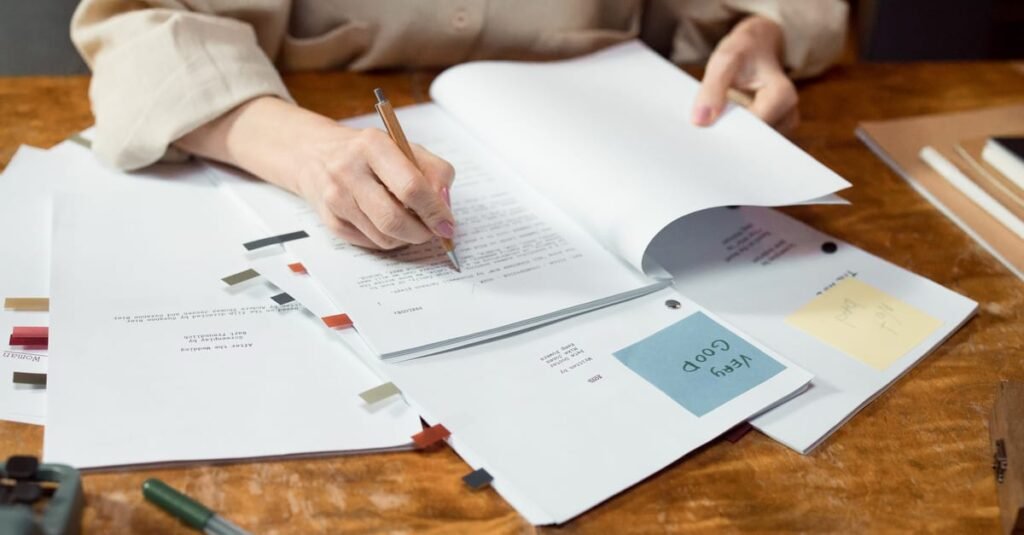Close-up of hands writing and organizing documents on a wooden desk.
